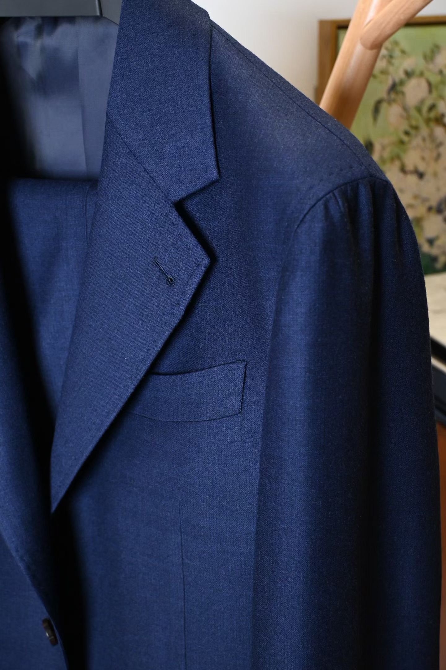 Navy jacket photographed on a hanger, showing notch lapel, buttonhole and chest pocket