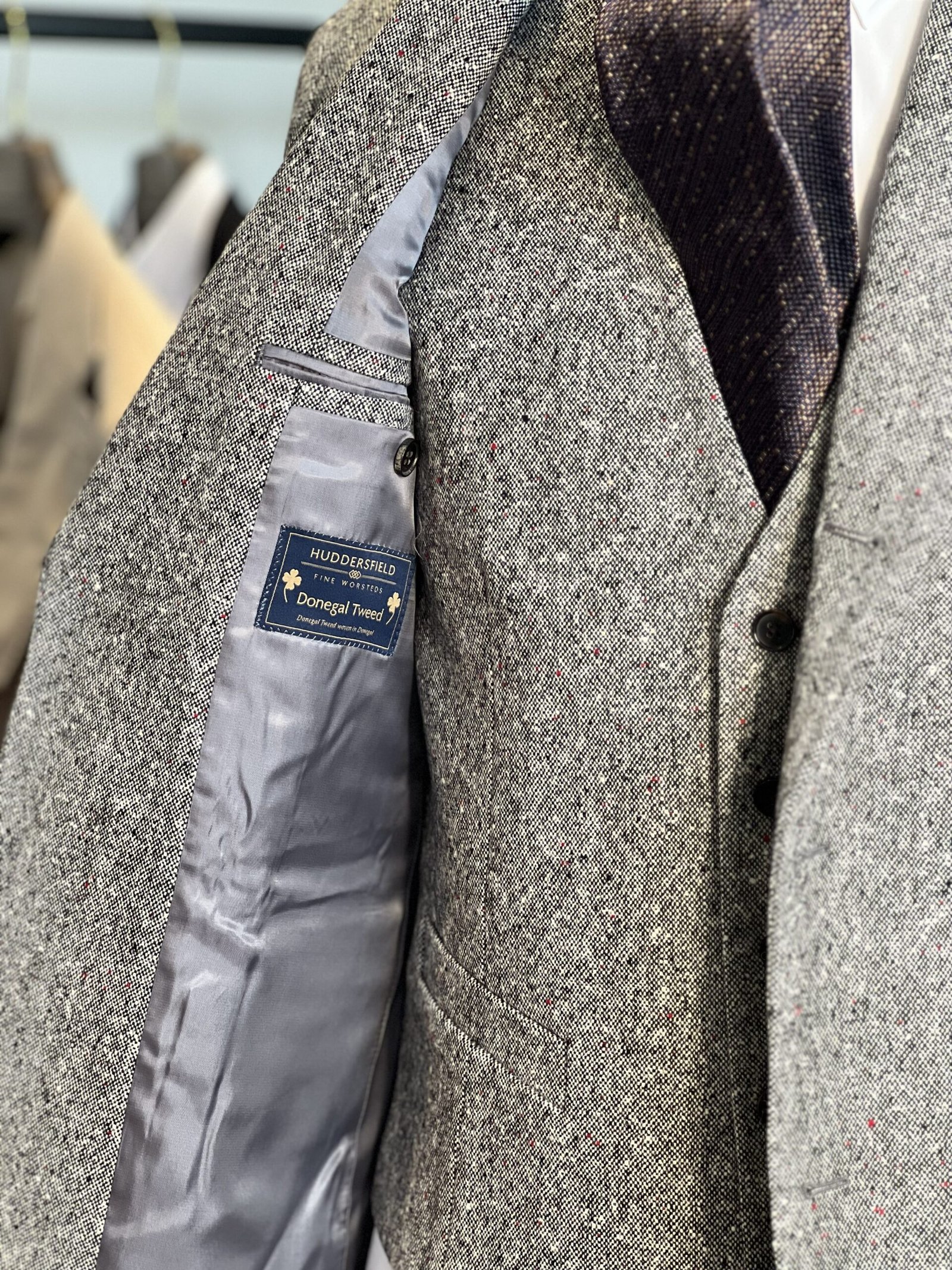 翻開的灰色外套內側布標，可見 Huddersfield Fine Worsteds 及 Donegal Tweed 字樣